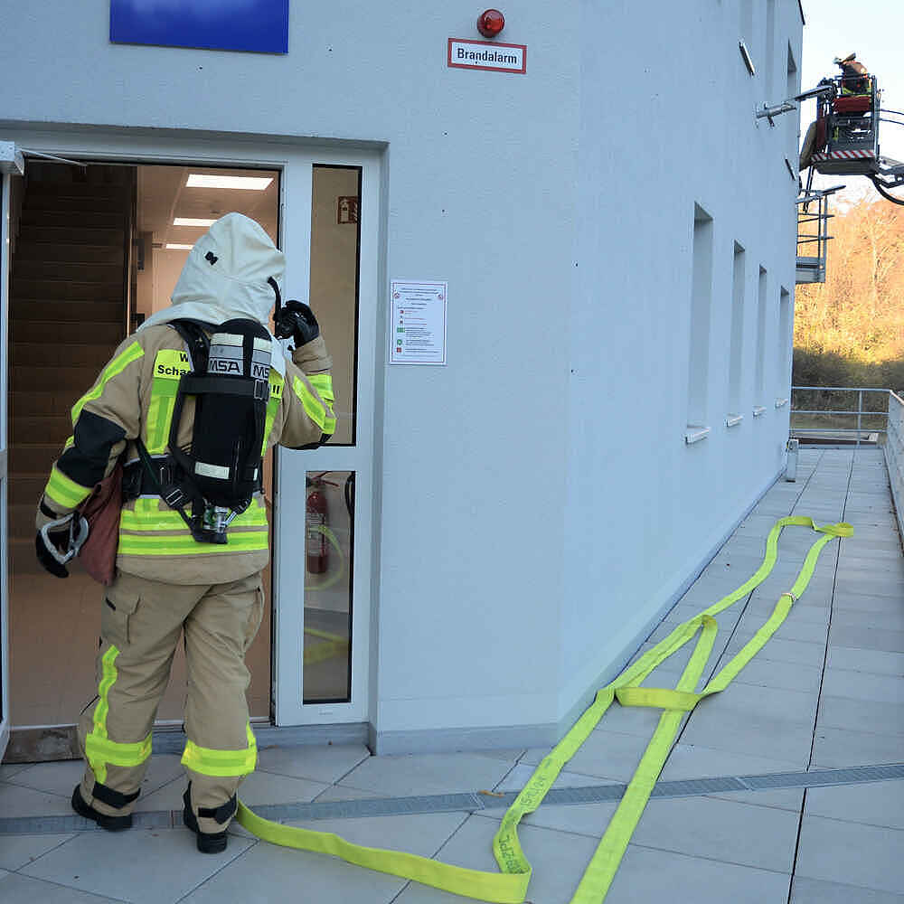 Ein Feuerwehrmann mit Atemschutz betritt ein Gebäude, an dessen Seite eine Drehleiter ausgefahren wird.
