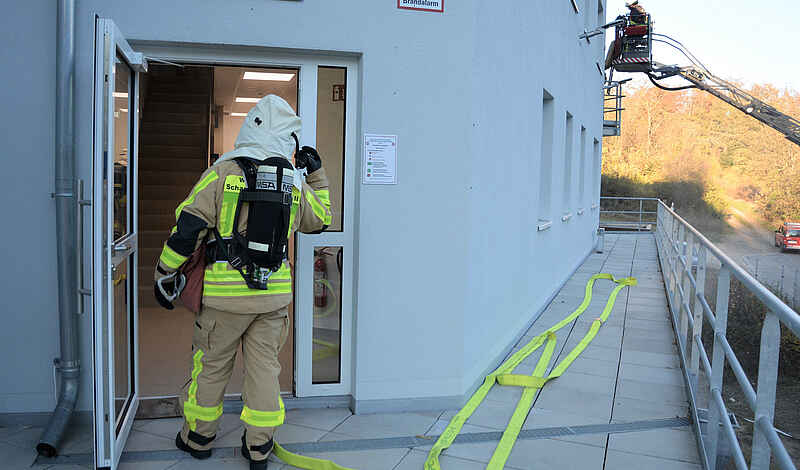 Ein Feuerwehrmann mit Atemschutz betritt ein Gebäude, an dessen Seite eine Drehleiter ausgefahren wird.