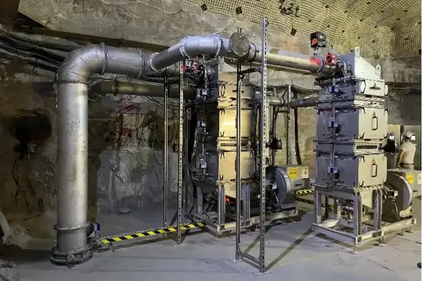 Das Bild zeigt die Abluftfilteranlage. Dabei handelt es sich um eine Konstruktion aus Metall, die aus einem großen Rohr sowie rechteckigen Kästen besteht.