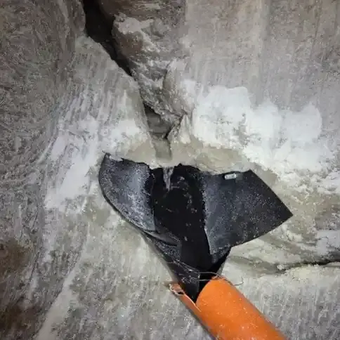 Das Foto zeigt eine Wand aus Salz mit einem Riss aus dem Salzwasser fließt. Um das Salzwasser aufzufangen, wird es über ein Stück schwarze Folie gezielt in ein orangenes Rohr geleitet.