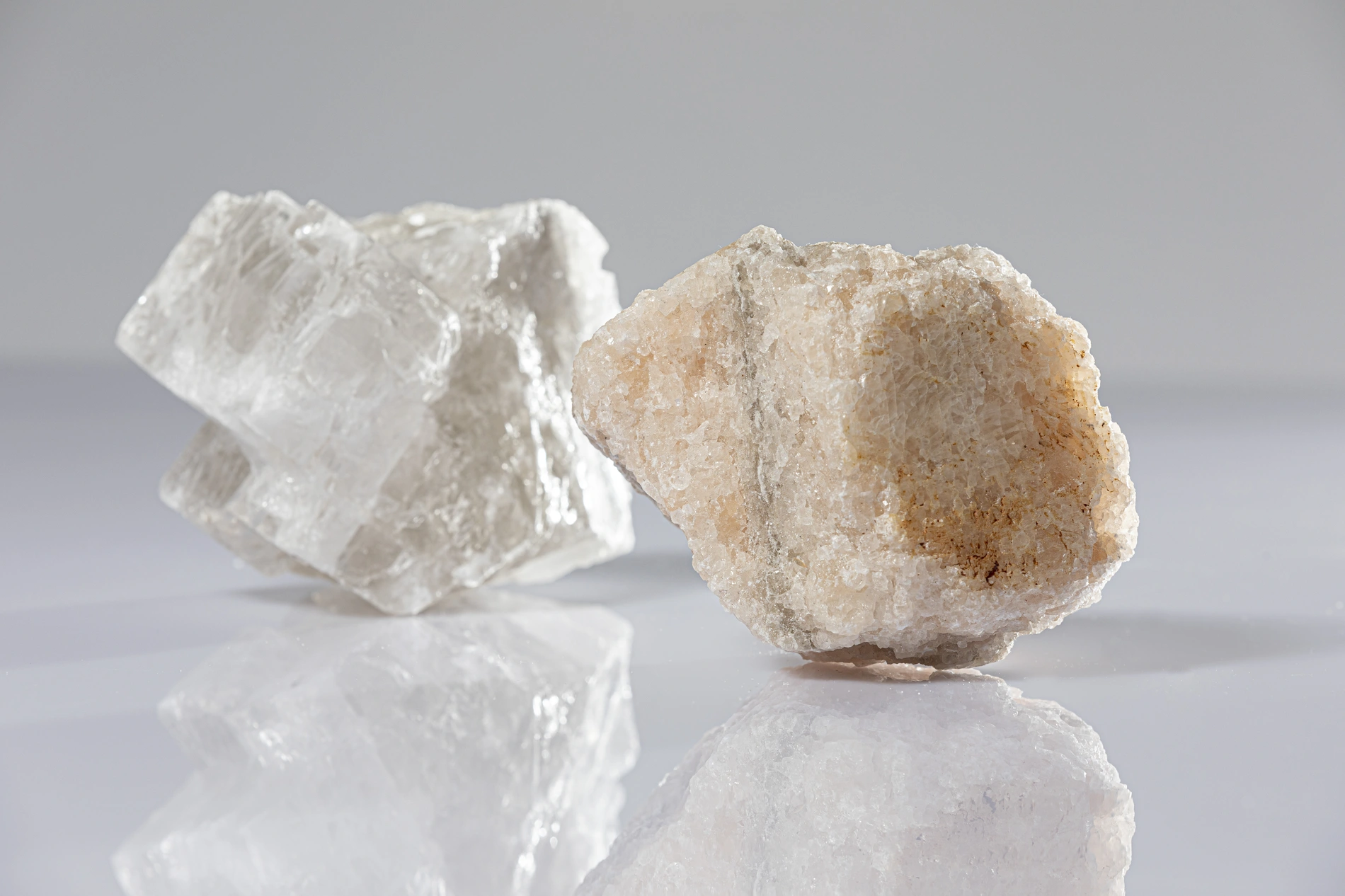 Two differently colored pieces of rock lie on a table, slightly reflected in its smooth surface.