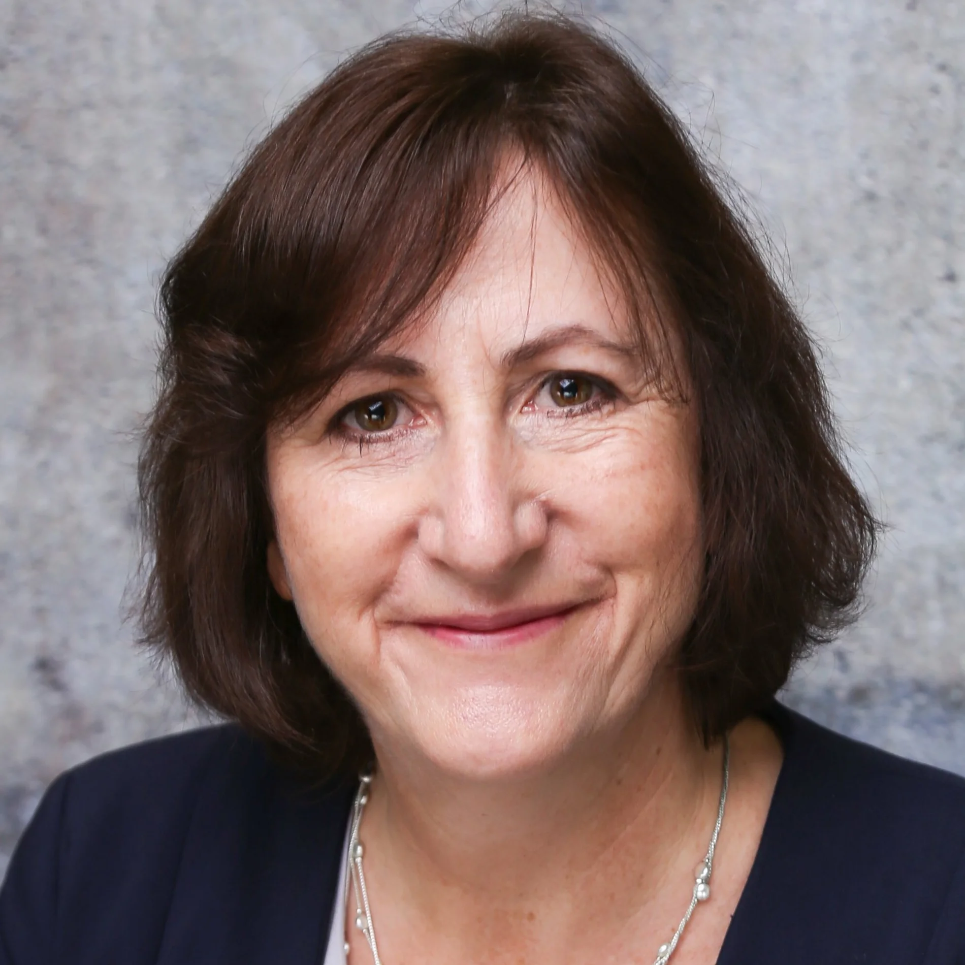 Porträtfoto einer Frau mit kinnlangen braunen Haaren. Sie lächelt in die Kamera und trägt eine silberfarbene Kette.