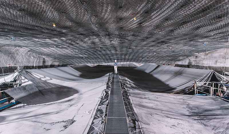 Speicherbecken unter Tage, das mit Planen abgedeckt ist. Auf einem Arbeitssteg in der Bildmitte steht im Hintergrund eine Person in Arbeitskleidung und Helm.