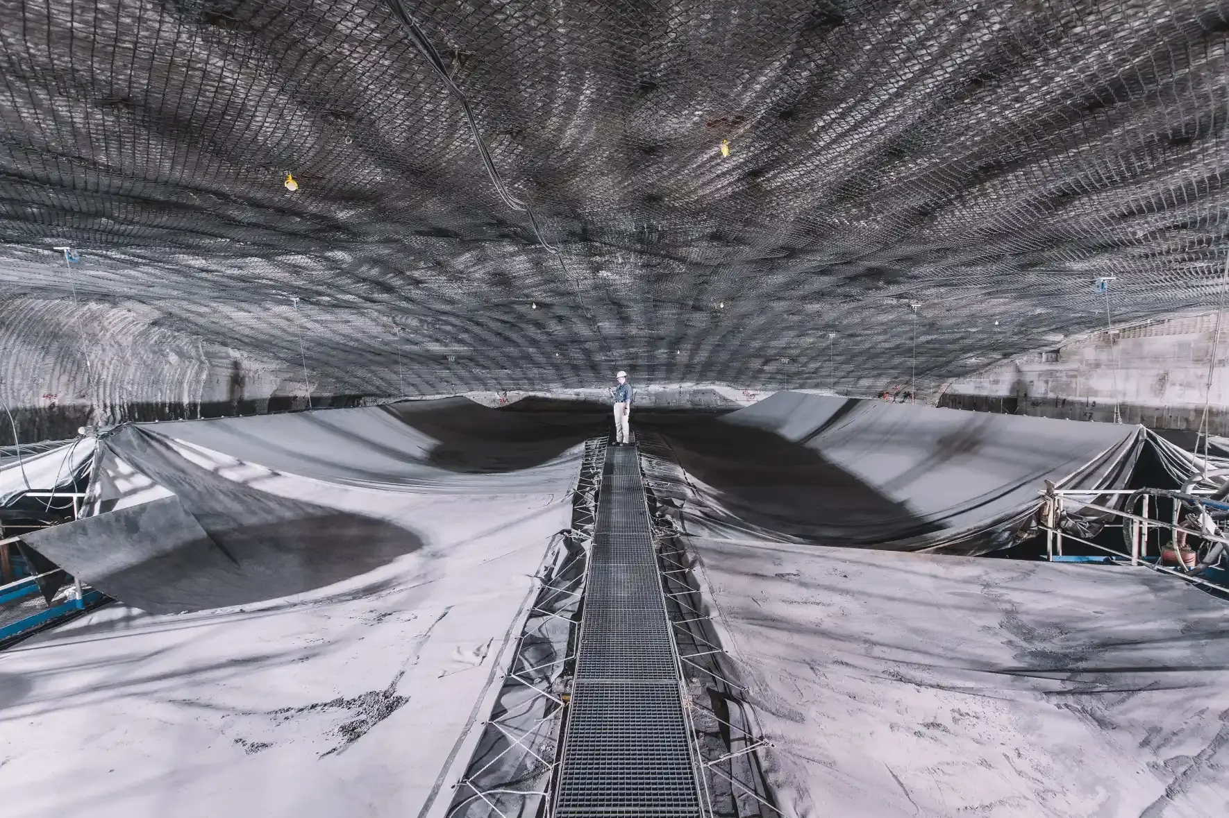 Speicherbecken unter Tage, das mit Planen abgedeckt ist. Auf einem Arbeitssteg in der Bildmitte steht im Hintergrund eine Person in Arbeitskleidung und Helm.