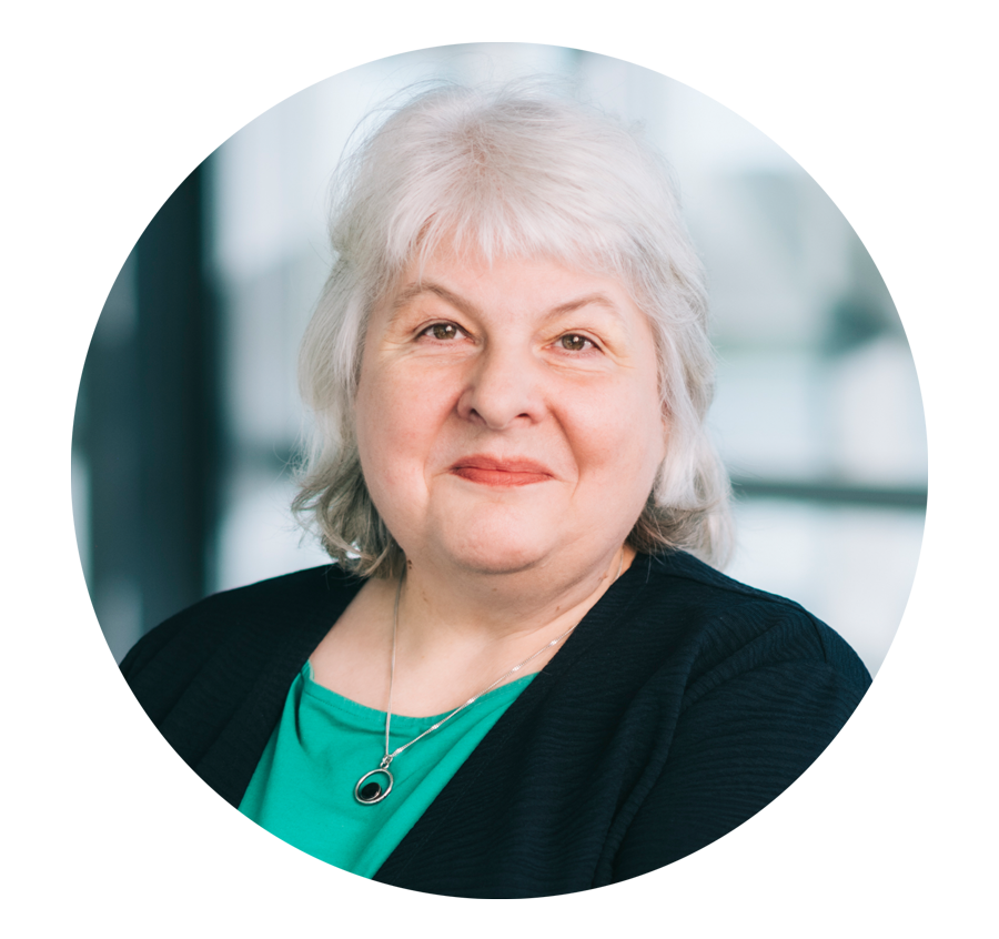 Porträtfoto: Eine Frau mit grauen schulterlangen Haaren lächelt in die Kamera. Sie trägt ein grünes Top unter einer schwarzen Jacke. 