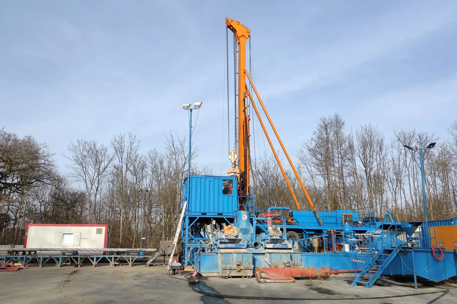 Eine blau-orangefarbene Bohranlage steht vor einen laublosen Wald