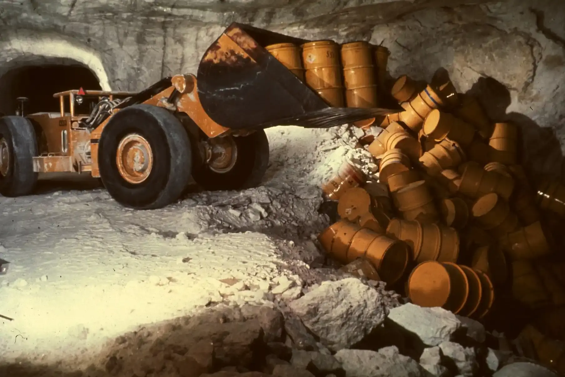 A wheel loader dumps barrels of radioactive waste.