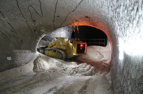 Eine gelbe Kettenraupe steht in einer Gabelung in einem Tunnel in einem Salzbergwerk und ver-dichtet das Salz, mit dem das Bergwerk wieder verfüllt wird (Stopfraupe).