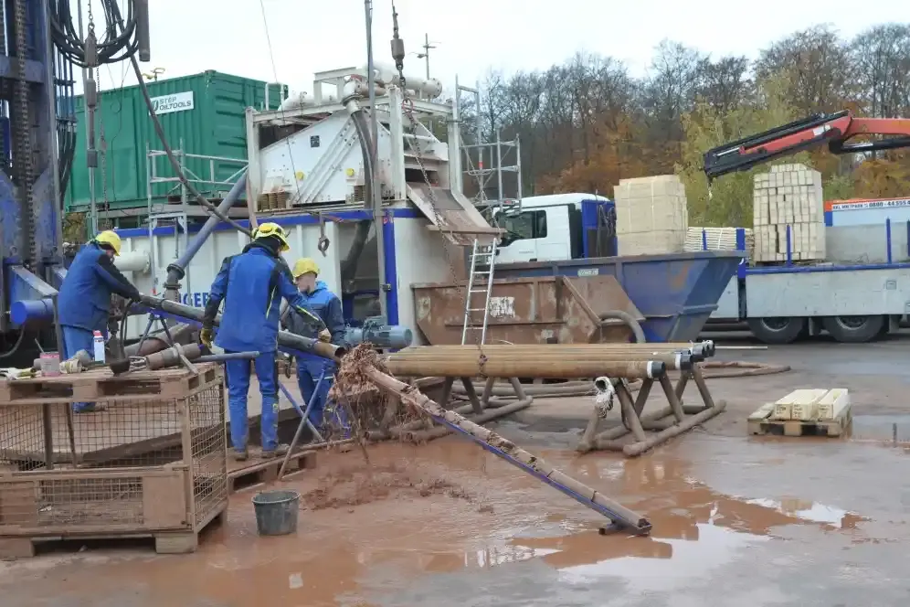 Drei Personen in blauer Arbeitskleidung spülen einen Bohrkern aus einem Rohr.