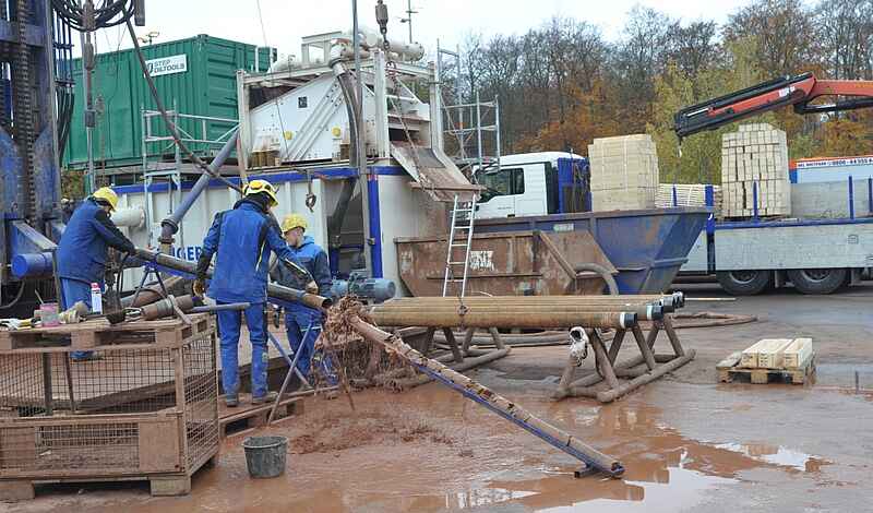 Drei Personen in blauer Arbeitskleidung spülen einen Bohrkern aus einem Rohr.