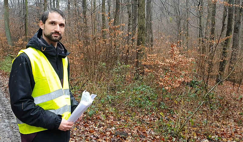 Ein Mann mit gelber Warnweste steht auf einem Waldweg.