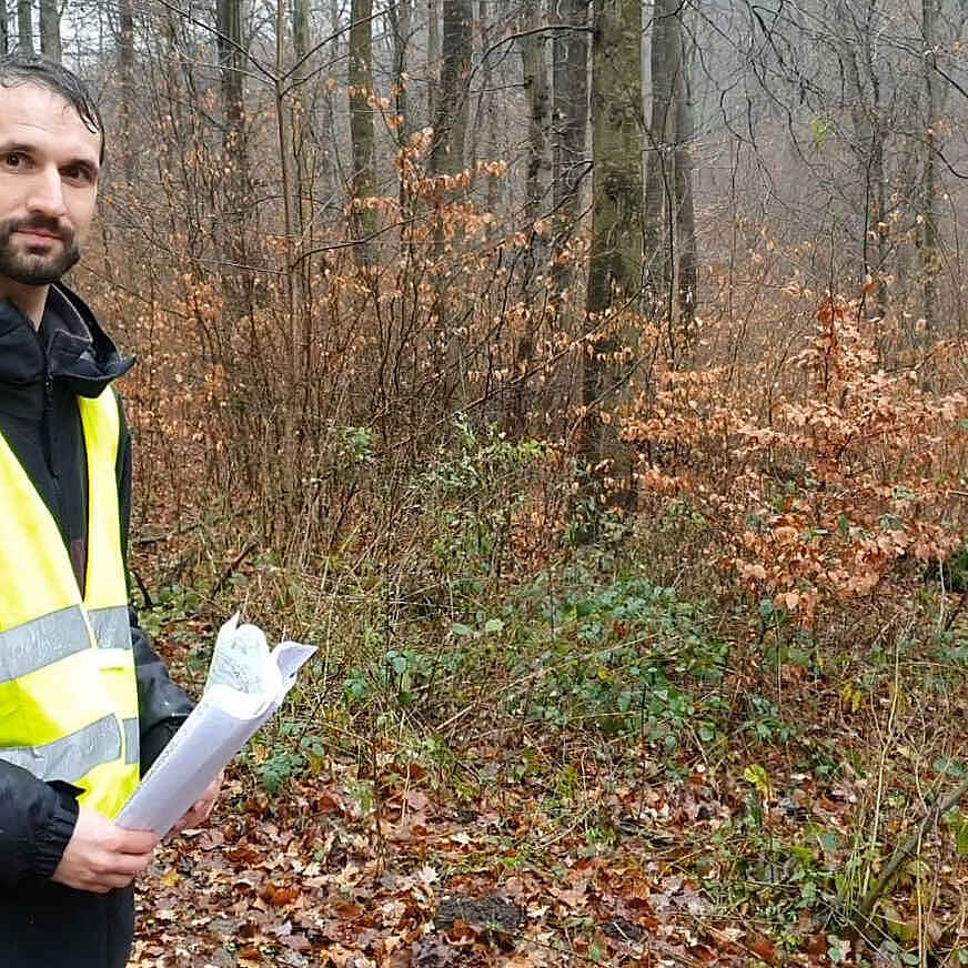 Ein Mann mit gelber Warnweste steht auf einem Waldweg.