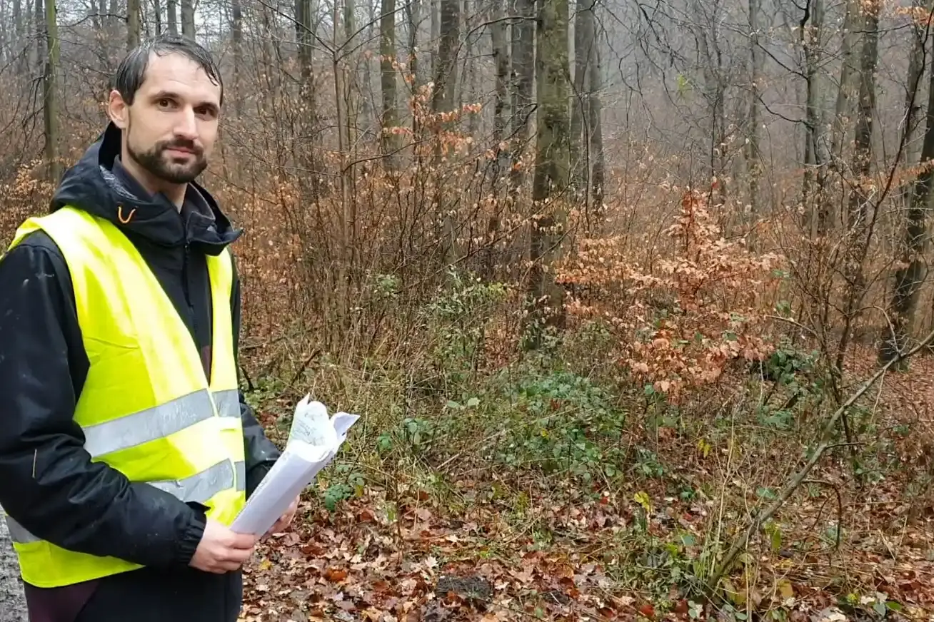 Ein Mann mit gelber Warnweste steht auf einem Waldweg.