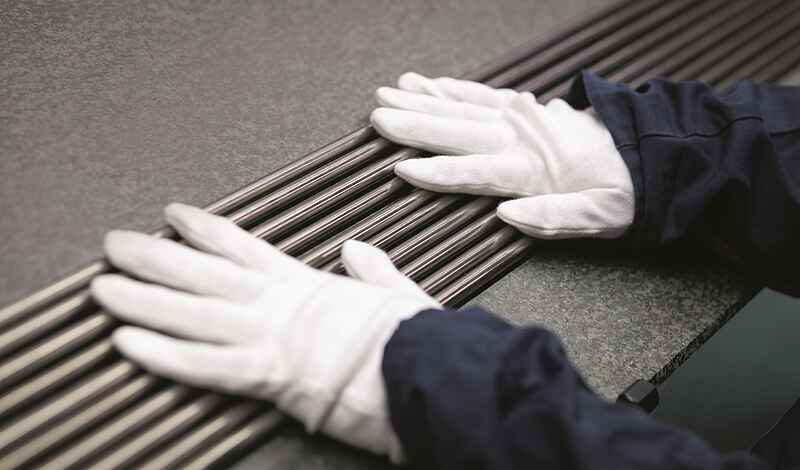 Zwei Hände in weißen Handschuhen liegen auf mehreren dicht beieinanderliegenden metallisch glänzenden Stäben.