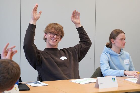 Ein Schüler der Berufsbildenden Schulen II in Gifhorn hebt die Hände und schaut zu einem Mitschüler. Neben ihm sitzt eine weitere Schülerin.