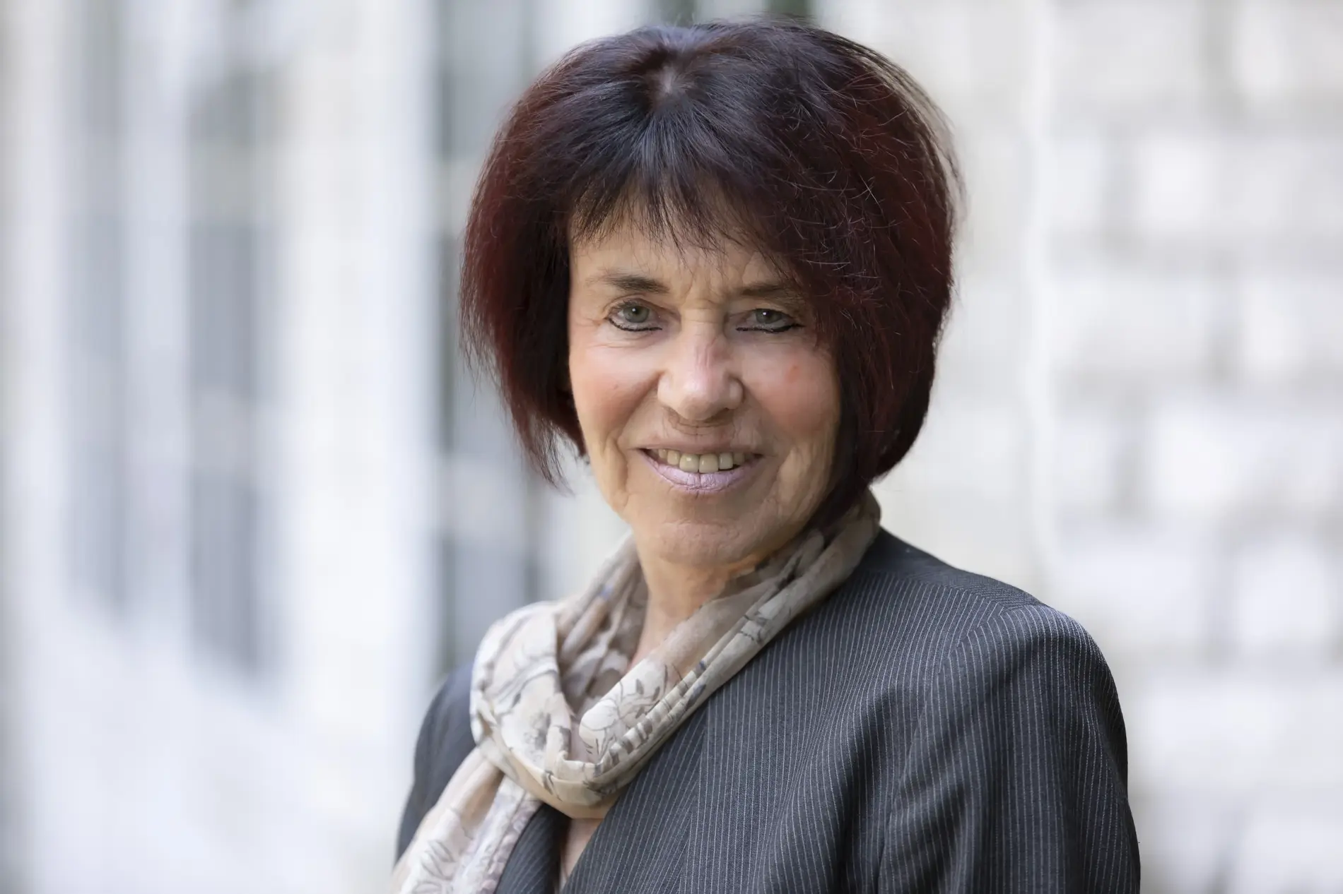 Eine Frau mit kinnlangen braunen Haaren lächelt freundlich in die Kamera. Sie trägt einen grauen Blazer und einen hellen gemusterten Schal. 