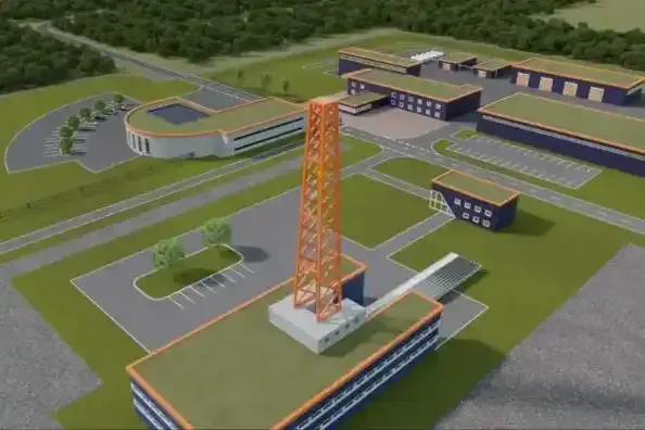 Luftaufnahme eines modernen Gebäudekomplexes mit markantem roten Turm, umgeben von Straßen, Parkplätzen und Grünflächen.