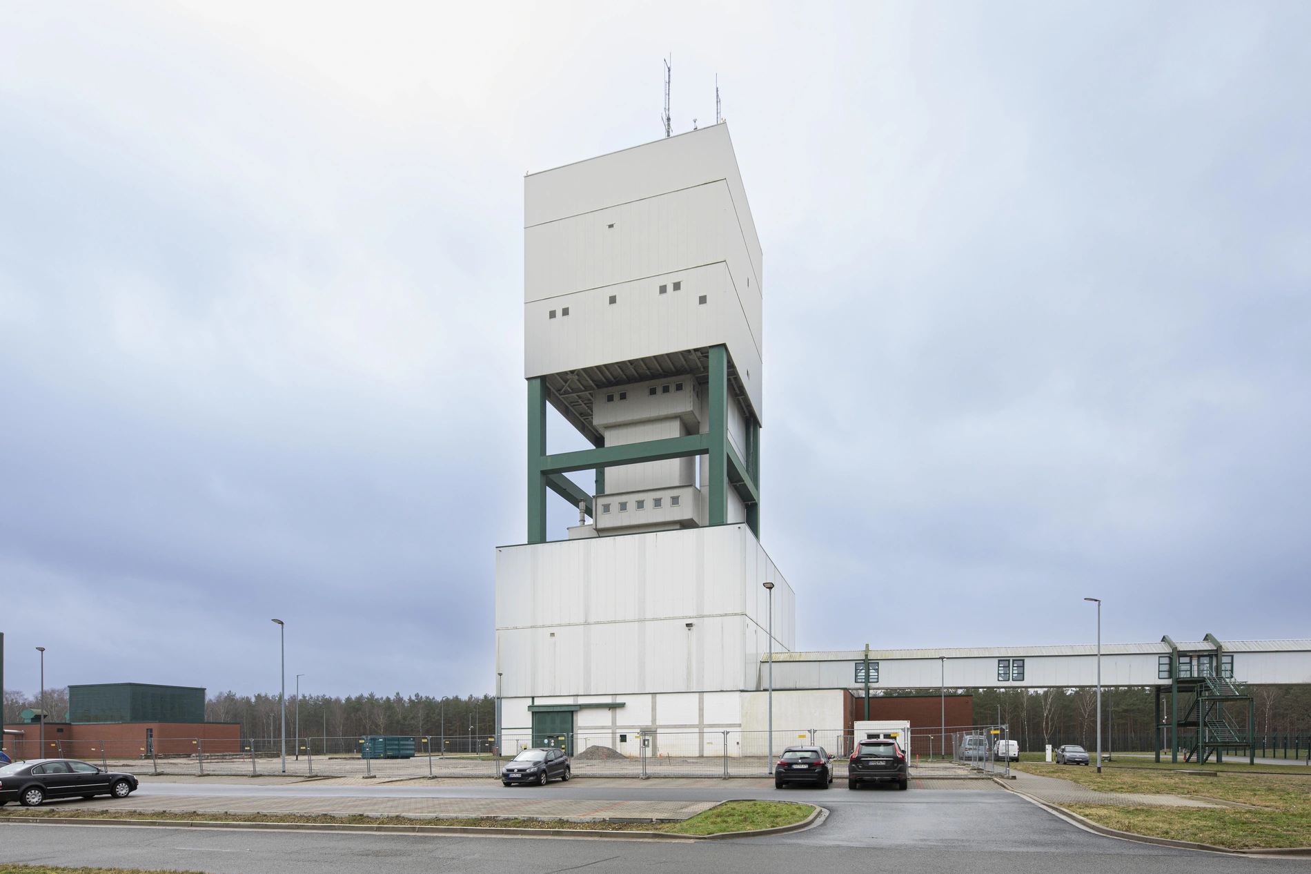 The winding tower of the Gorleben mine - photographed from the parking lot in front of it, where a few cars are parked.