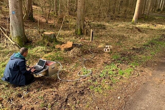 Ein Mann hockt mit einem Laptop im Wald