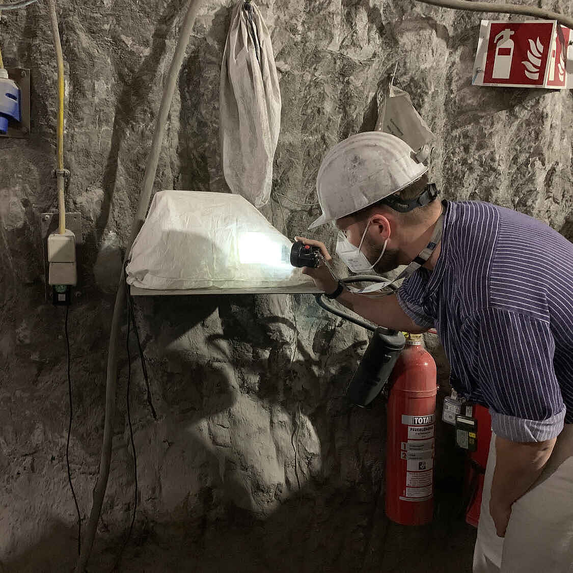 Ein Bergarbeiter schaut unter Tage auf eine Messgerät, das an einer Bergwand installiert ist.
