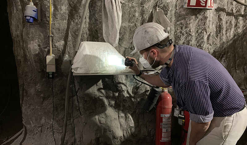 Ein Bergarbeiter schaut unter Tage auf eine Messgerät, das an einer Bergwand installiert ist.