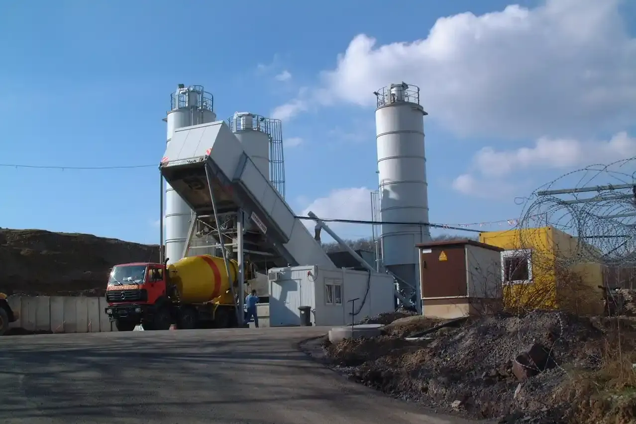 Ein LKW steht neben einem Baucontainer. Im Hintergrund stehen weitere Container und drei Silos.  " title="Der Salzbeton für die bGZ-Maßnahme wurde vor Ort in einer Mischanlage hergestellt.