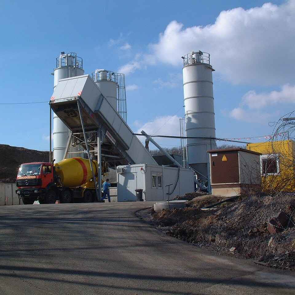 Ein LKW steht neben einem Baucontainer. Im Hintergrund stehen weitere Container und drei Silos.  " title="Der Salzbeton für die bGZ-Maßnahme wurde vor Ort in einer Mischanlage hergestellt.