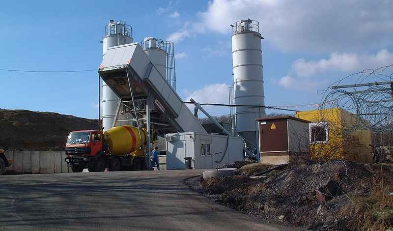 Ein LKW steht neben einem Baucontainer. Im Hintergrund stehen weitere Container und drei Silos.  " title="Der Salzbeton für die bGZ-Maßnahme wurde vor Ort in einer Mischanlage hergestellt.