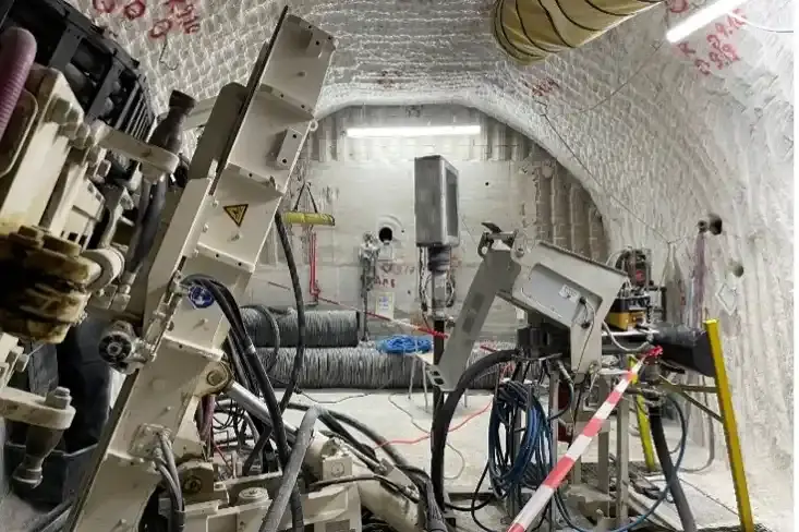 Das Bild zeigt eine Maschine unter Tage. Hinter der Maschine befindet sich eine Betonmauer. In der Betonmauer befindet sich eine runde Öffnung.