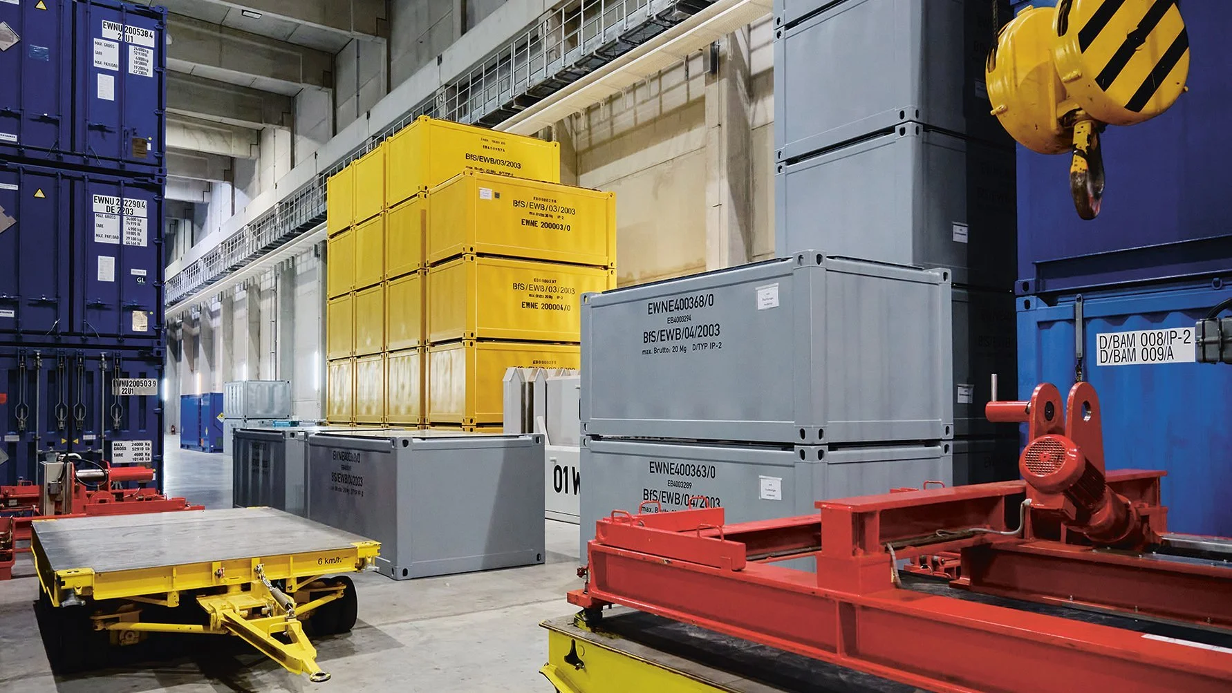 Mehrere Container in gelb, grau und blau in einer großen Halle.