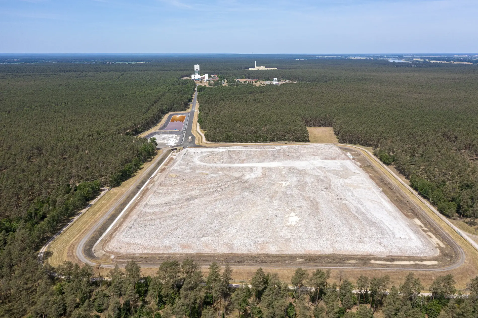 The square salt heap of the Gorleben mine - photographed from the air. The mine's winding tower, to which a road leads, can be seen in the background. Huge areas of forest stretch out all around. 