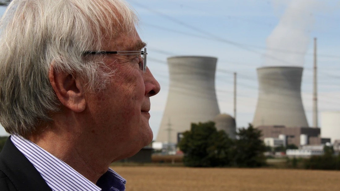 Portraitfoto in Seitenansicht von Raimund Kamm, einem Mann mit Hemd und weißen Haaren und Brille, mit zwei Kühltürmen im Hintergrund