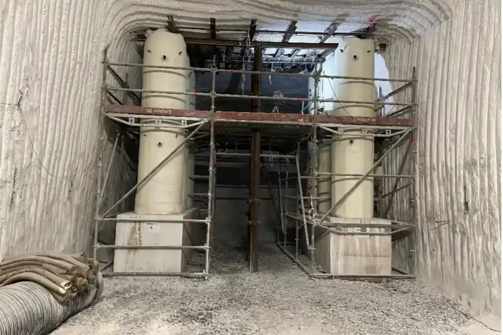 In einer Strecke unter Tage steht ein Bauwerk in einer Nische. Rechts und links stehen Säulen aus Beton gefüllten Säcken auf Quadern aus Beton. Direkt unter der Decke liegen Stahlträger auf den Säulen. Ein Metallgerüst umgibt das Bauwerk.