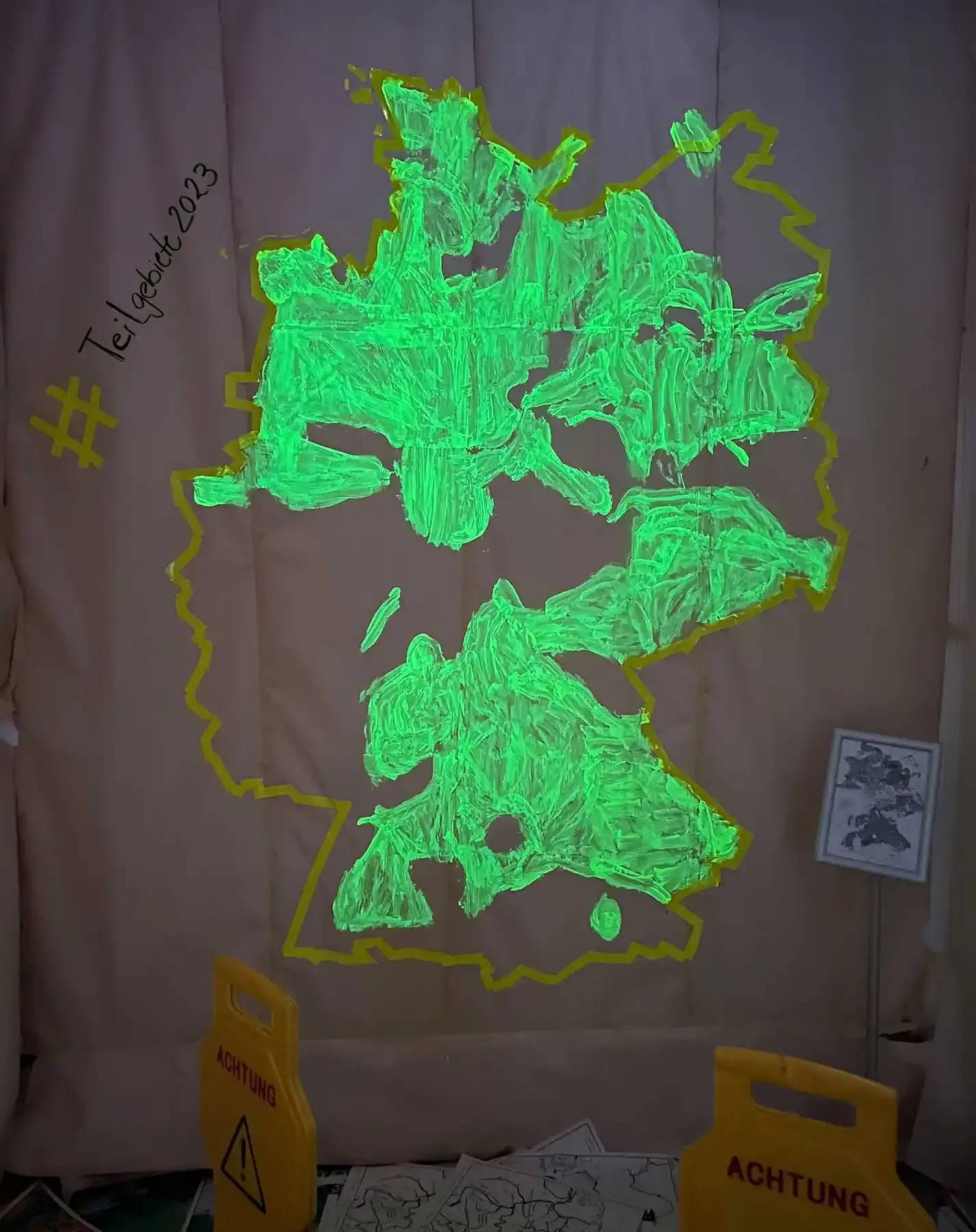 Auf eine mit Packpapier verkleidete Wand ist eine große Deutschlandkarte gemalt. Innerhalb der Deutschlandkarte befinden sich mit fluoreszierender Farbe eingefärbte Flächen. 