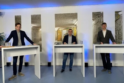 Drei Männer stehen nebeneinander an Stehtischen und sehen in die Kamera
