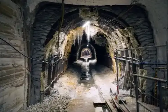 Foto einer Strecke unter Tage. In dem tunnelartigen Gewölbe verläuft ein salzverkrustetes Rinnsal, an der Decke wachsen Salzstrukturen.