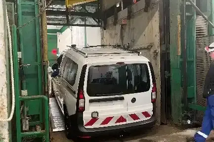 1.	Ein weißes Fahrzeug steht auf einer niedrigen Rampe in einem Förderkorb