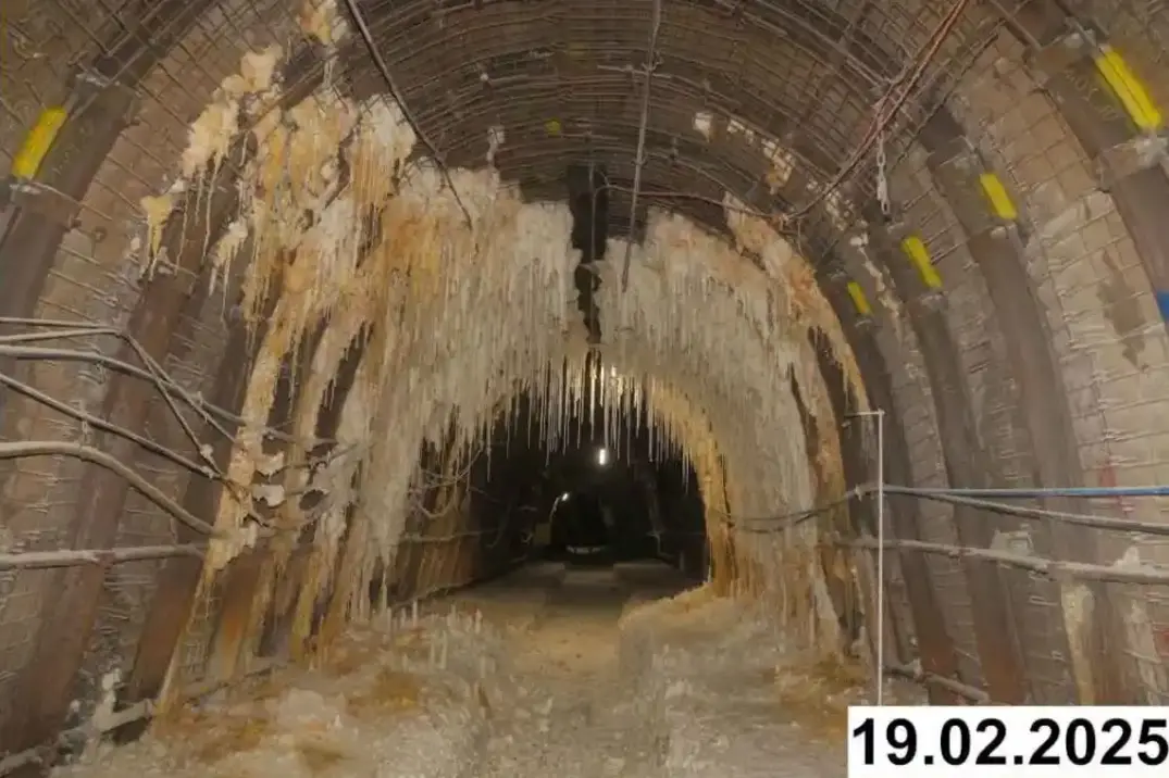 Foto einer bogenförmigen Strecke unter Tage. An den Seiten und der Decke bilden sich weiße Verkrustungen.