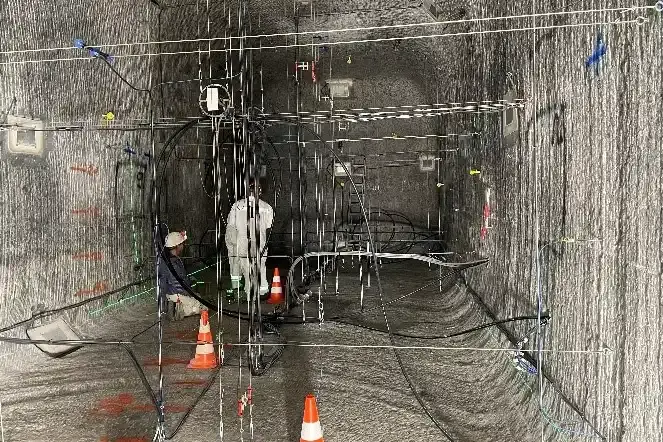 Foto einer Strecke unter Tage in einem Salzbergwerk. Senkrecht und waagerecht verlaufen Stahlseile und Kabel. Im Hintergrund sind zwei Personen in Arbeitskleidung zu erkennen.
