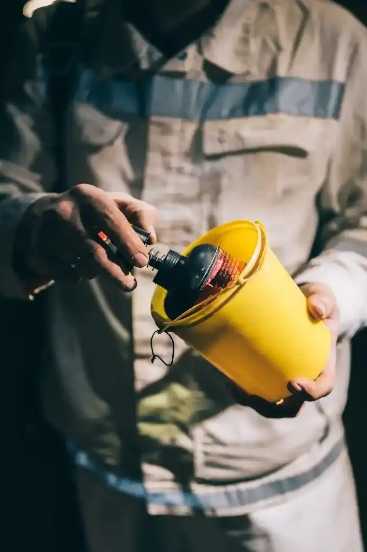 Eine Person in weißer Schutzkleidung zieht aus einer gelben Dose ein schwarzes Messgerät heraus.