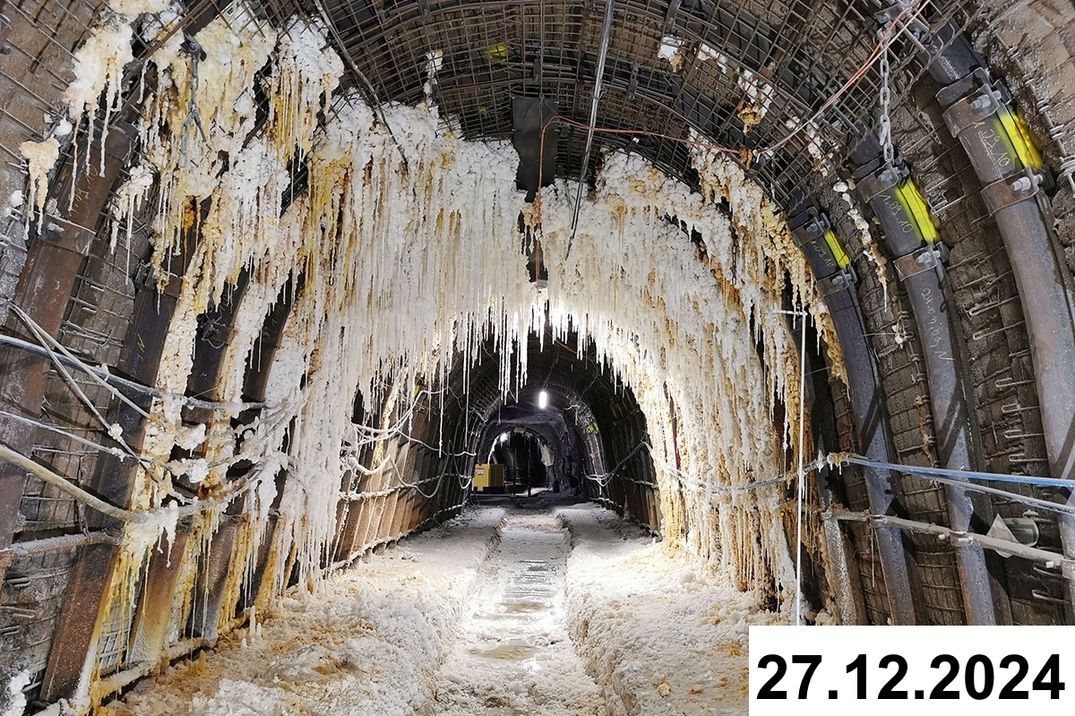 Foto einer bogenförmigen Strecke unter Tage. An den Seiten und der Decke bilden sich weiße Verkrustungen.