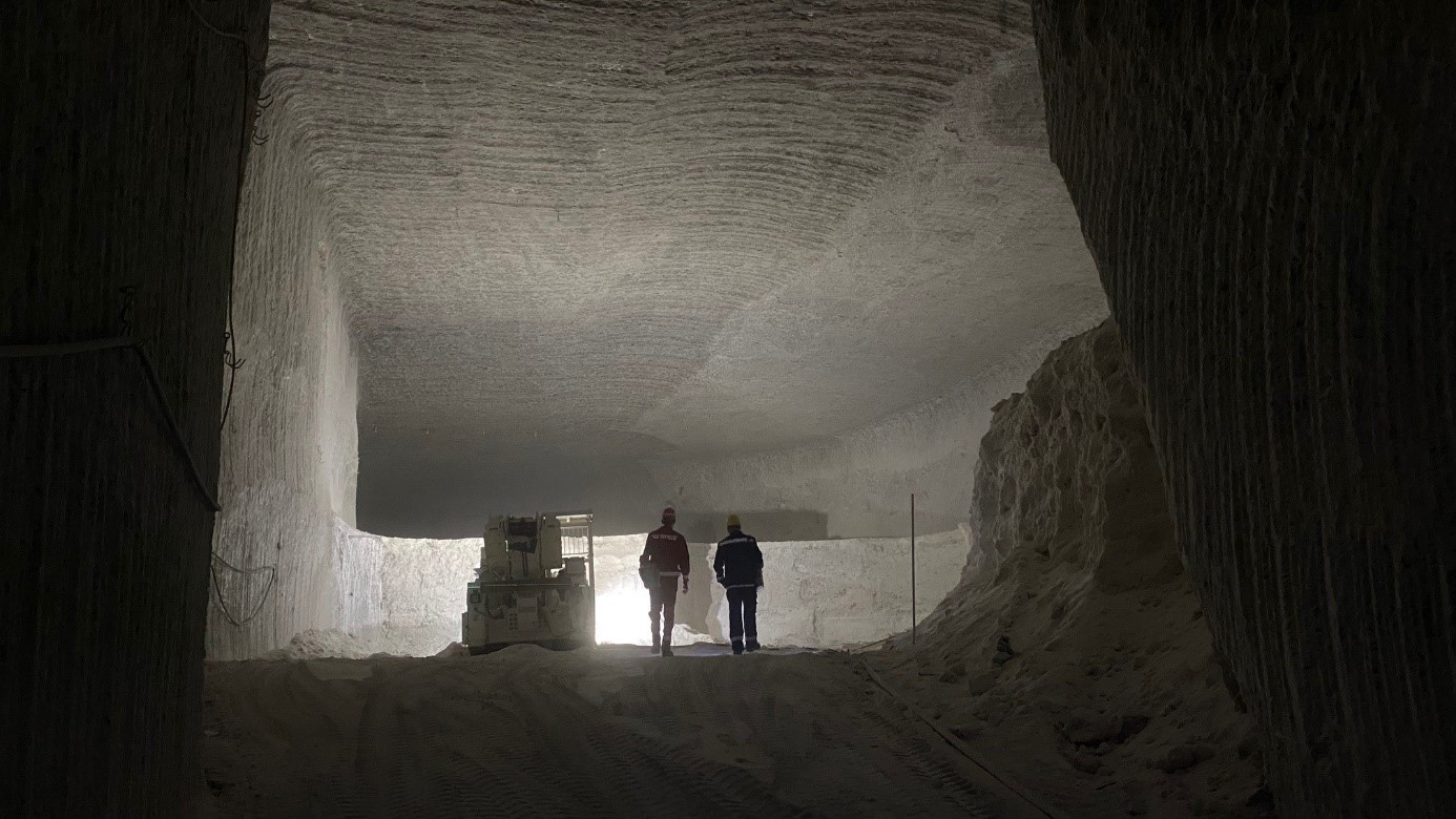 Zwei Bergleute auf dem Weg in eine Abbaukammer, die von den Scheinwerfern eines Fahrladers erleuchtet wird. 