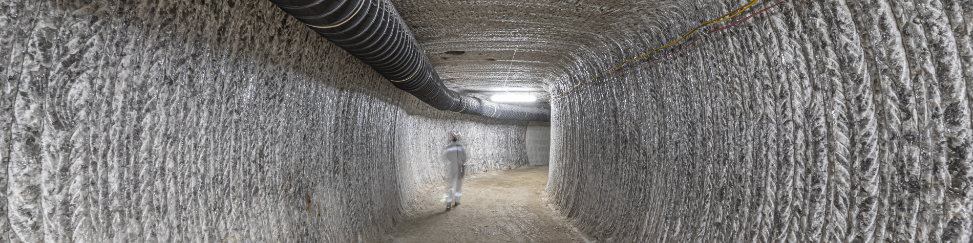 Blurred person in miner's clothing from behind, walking down a long shaft.