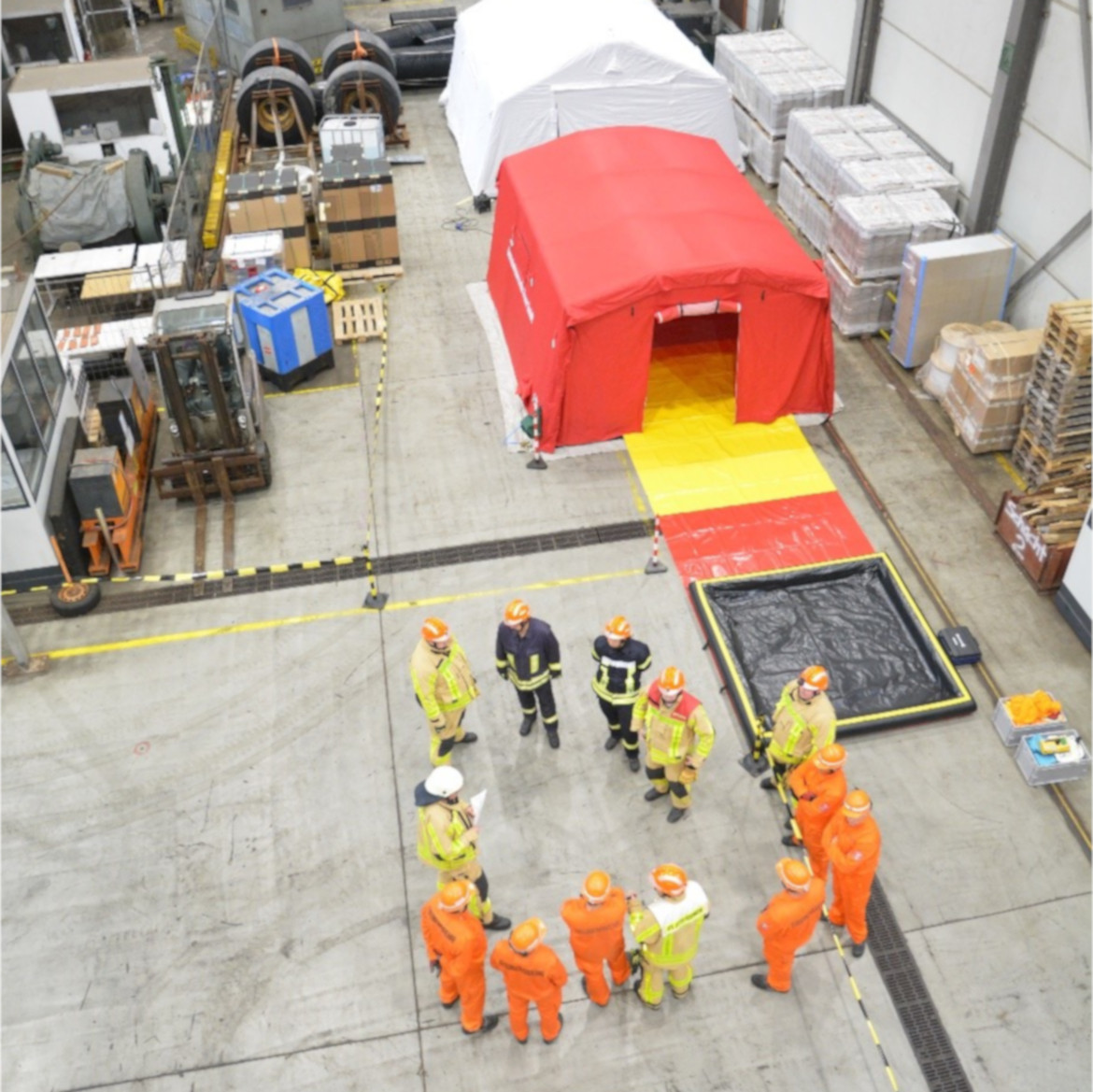 Zusammenarbeit von Betriebsfeuerwehr und Grubenwehr der Schachtanlage Asse II in der Schachthalle Im Hintergrund sieht man den Aufbau von Dekontaminationsanlagen und –zelten. Sollte es zu einer möglichen Freisetzung radioaktiver Stoffe bei einem untertägigen Zwischenfall kommen, muss verhindert werden, dass Kolleginnen und Kollegen beim Räumen der Grube von dort radioaktive Verunreinigungen verschleppen. Also leitet die Feuerwehr mit Unterstützung der Grubenwehr alle Personen, die das Bergwerk verlassen in gesonderte Bereiche, in denen sie auf Kontamination geprüft und bei Bedarf auch dekontaminiert werden können.