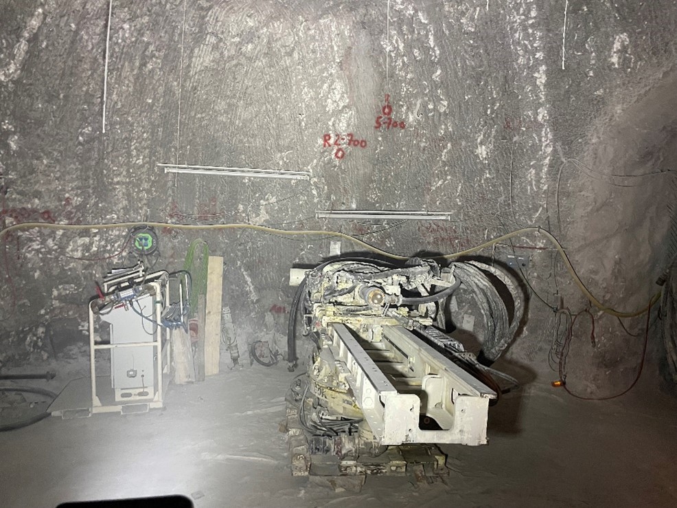 Eine weiße Metallkonstruktion mit Schläuchen steht unter Tage in einem Bergwerk. Die Wände sind dunkelgrau und an ihnen verlaufen weitere Kabel und Schläuche.