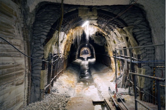 Foto einer Strecke unter Tage. In dem tunnelartigen Gewölbe verläuft ein salzverkrustetes Rinnsal, an der Decke wachsen Salzstrukturen.