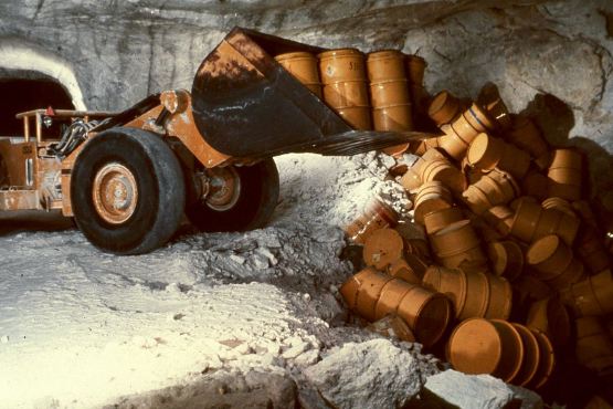 Ein Radlader lädt 1975 in einer Kaverne des Salzbergwerkes Asse Fässer mit radioaktivem Abfall ab. Underground: an excavator tilts barrels on a pile.