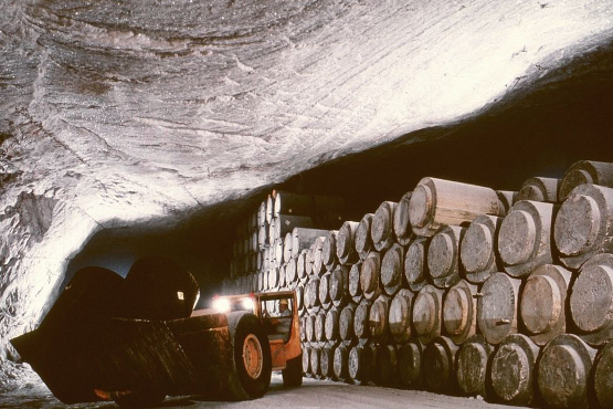 In einer Kaverne des Salzbergwerkes Asse gelagerte Fässer mit radioaktivem Abfall. Underground: lying stacked barrels – coated with concrete – in front of it a large excavator.