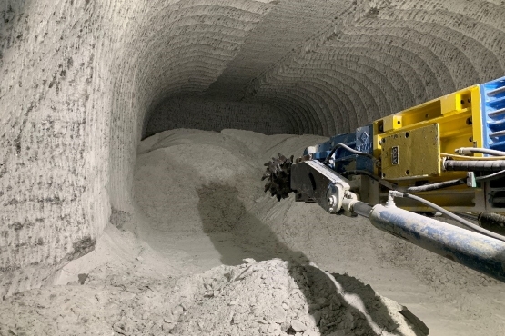 Es ist ein Hohlraum unter Tage im Salzbergwerk zu sehen. In dem Hohlraum liegt grobes Salzmaterial. Im Vordergrund ist ein Teil einer Fräse zu sehen, mit der im Salzgestein Hohlräume errichtet werden können.