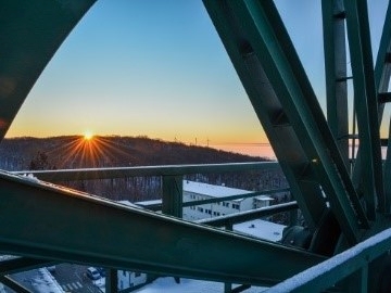 Foto eines winterlichen Sonnenaufgangs, fotografiert durch die Speichen eines großen Metallrads.